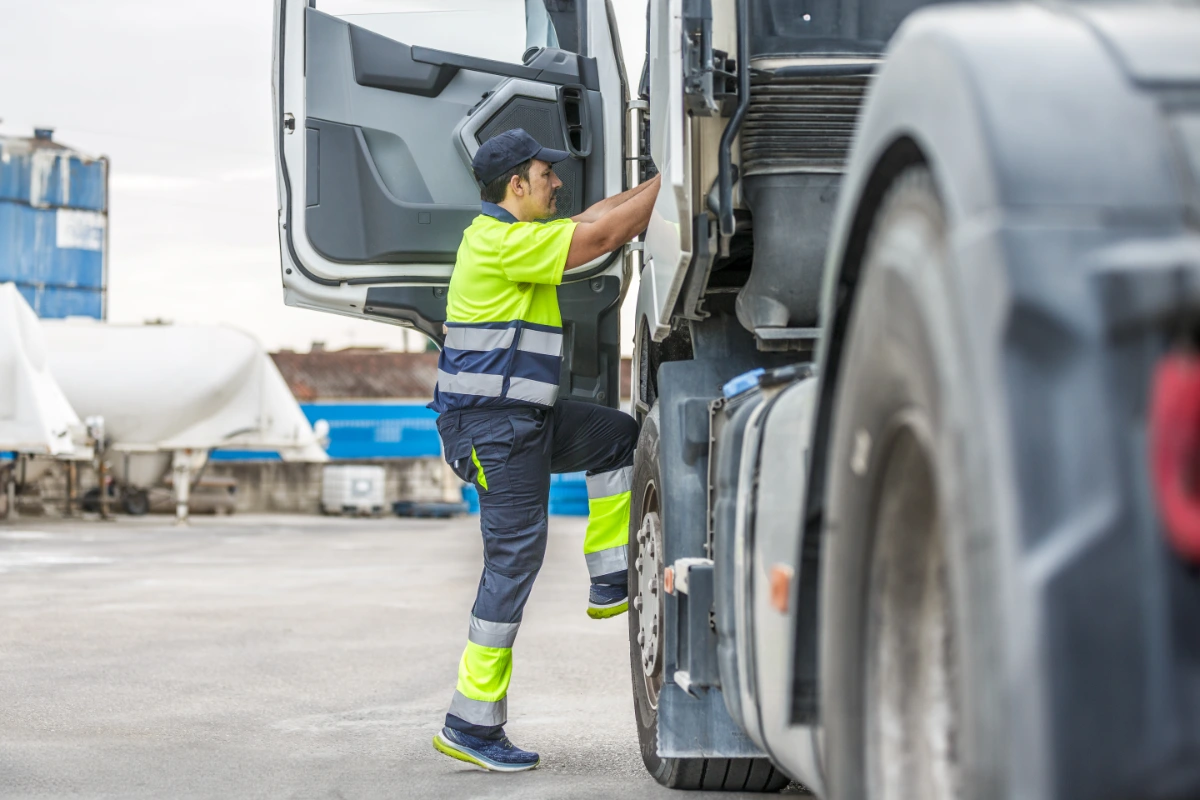 HGV driver in high-visibility clothing climbing into a lorry cab