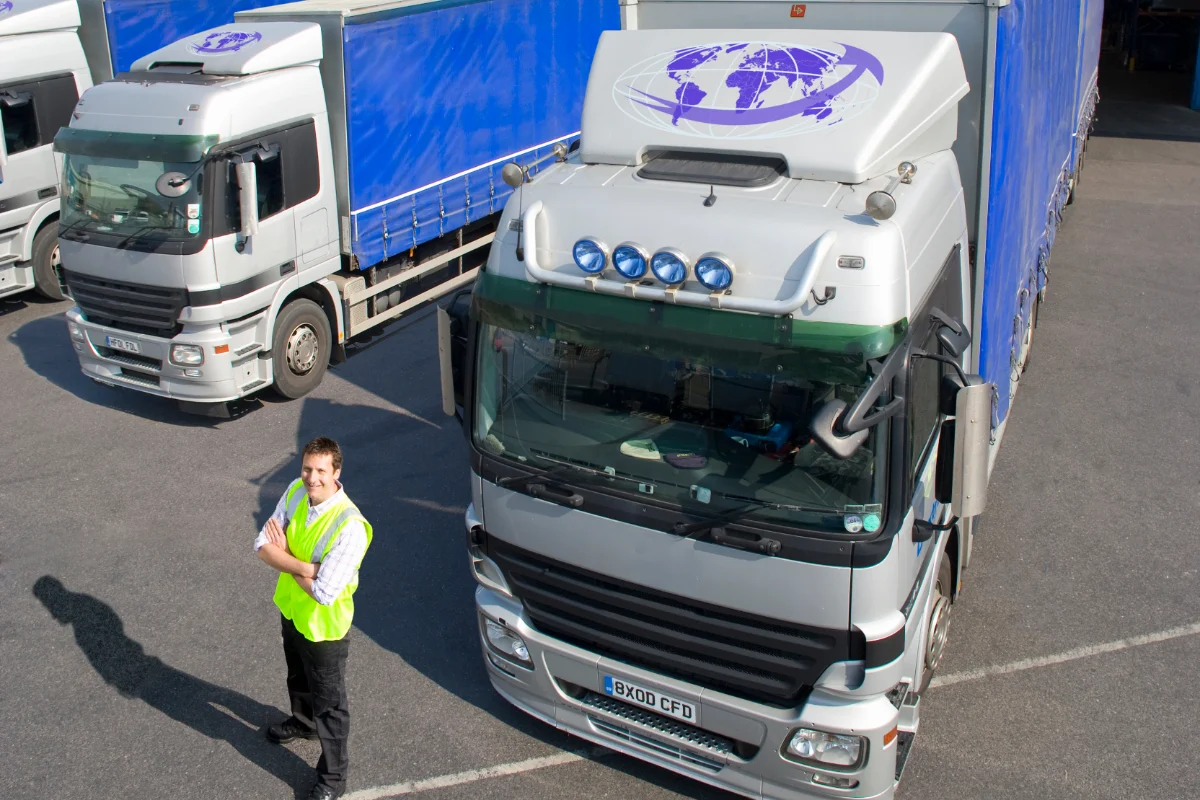 Logistics manager standing beside a fleet of commercial delivery lorries