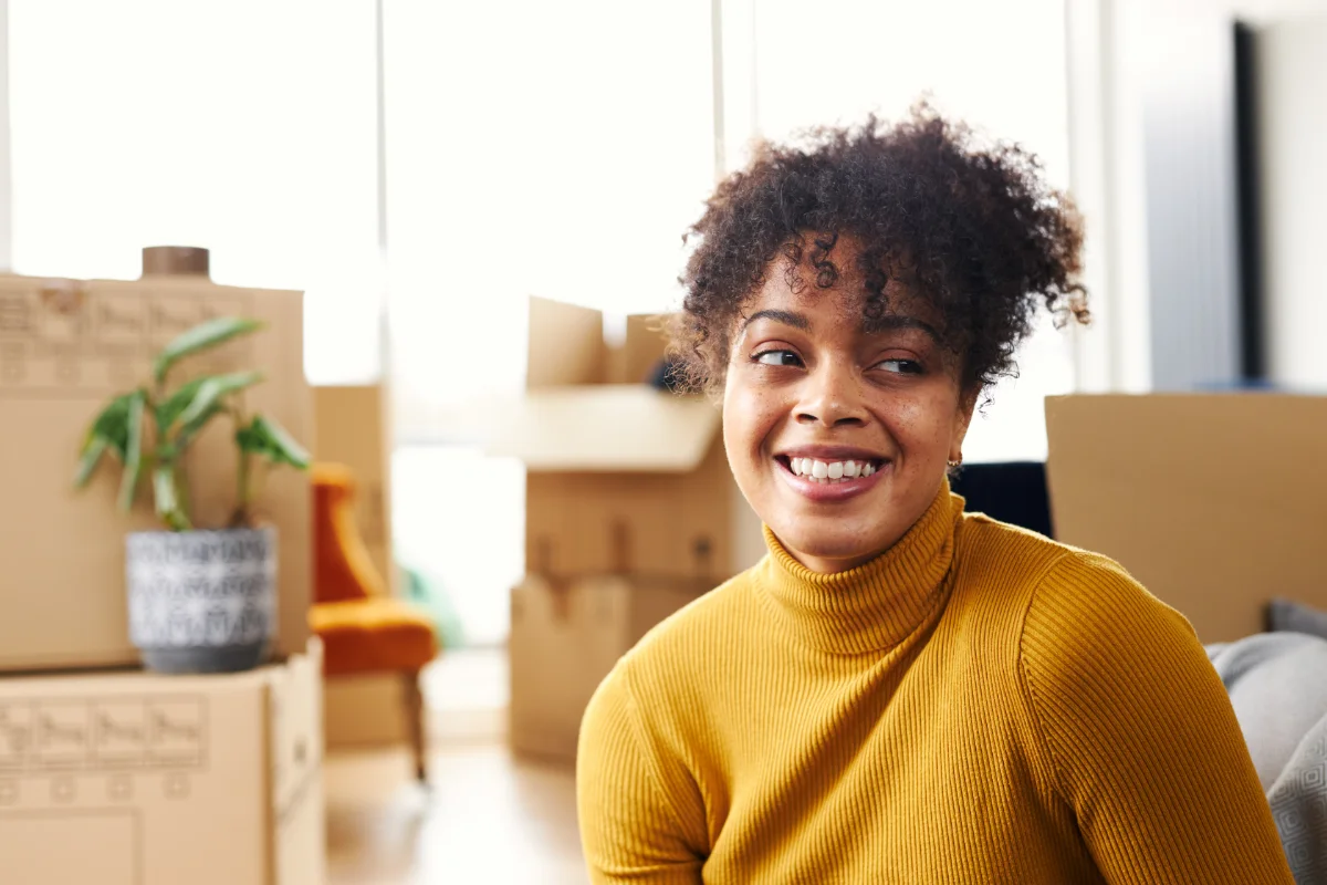 Smiling woman sitting in a new home surrounded by moving boxes