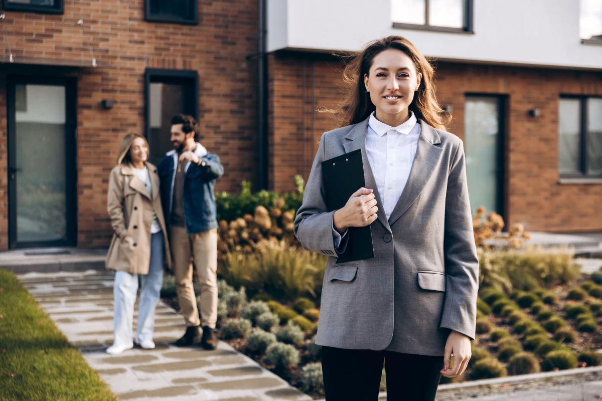 Female property professional standing outside a modern home with prospective buyers